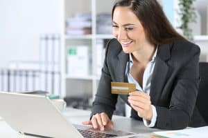 Smiling businesswoman holding credit and making payment from her laptop
